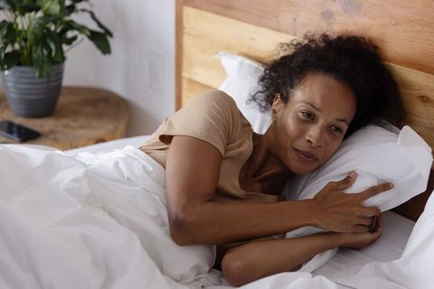 African american woman relaxing in cozy bed hugging pillow, morning wellness and restful comfort