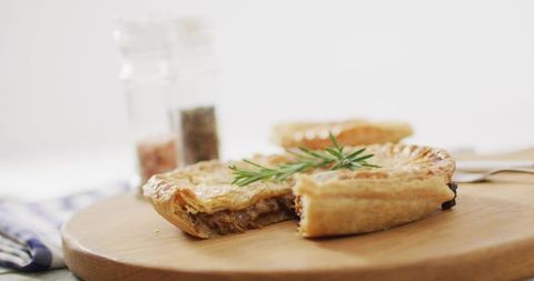 Savory meat pie with golden flaky crust and rosemary garnish on wooden board