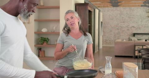 Diverse couple cooking together in openplan loft kitchen woman mixing batter at island