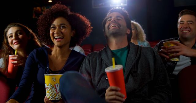 Young adults laughing and enjoying a movie together at the cinema while holding popcorn and drinks. Perfect for content related to entertainment, social outings, cinema experiences, happiness, and bonding with friends.