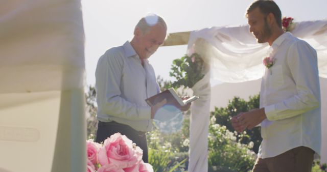 Officiant joyfully conducting wedding ceremony in serene outdoor venue with groom. Flowers enhance the romantic atmosphere. Suitable for wedding planning, love, celebration, romance, outdoor ceremonies, and marriage services promotions.