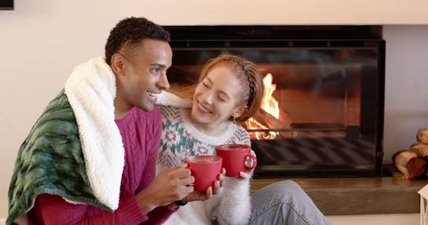 Smiling Couple Enjoying Cozy Moment by Fireplace with Hot Beverages