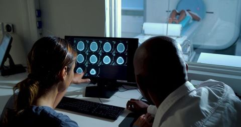 Medical team reviewing brain mri scans in control room while patient undergoing mri scan