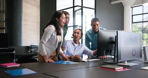 Diverse Team Celebrating Success Around Computer in Modern Office