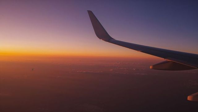 Airliner wing silhouetting over sunset horizon from cabin window