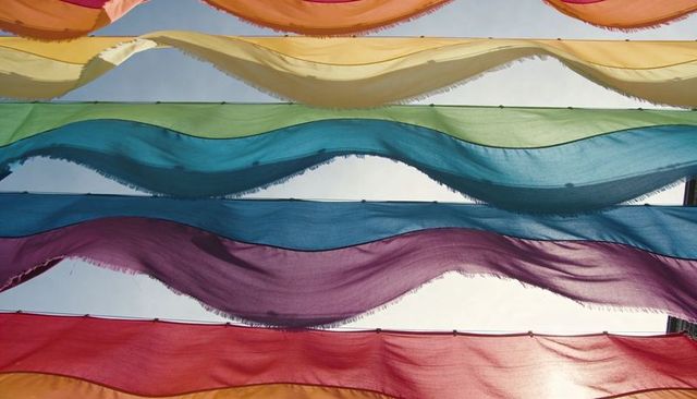 Waving sheer fabric panels forming rainbow translucent canopy across sunlit courtyard