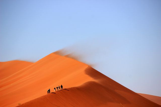 Group of hikers traversing red sand dunes, perfect for depicting adventure travel, exploration, arid landscapes, and nature excursions. Ideal for travel brochures, adventure tourism advertising, nature magazines, and hiking gear promotions.