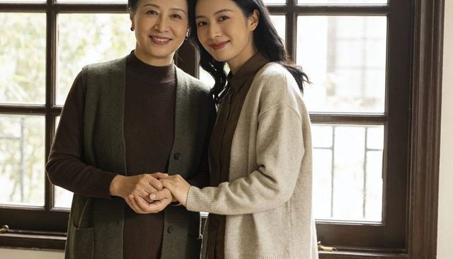 Smiling mother and daughter holding hands by backlit window, warm family connection