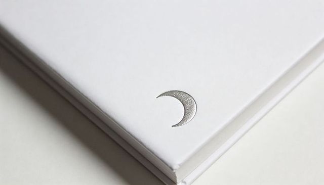 Minimalist white notebook with silver crescent embossing on clean stacked pages, monochrome