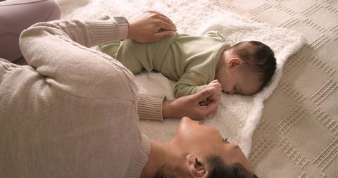 Mother enjoying tender moment with sleeping baby on soft blanket