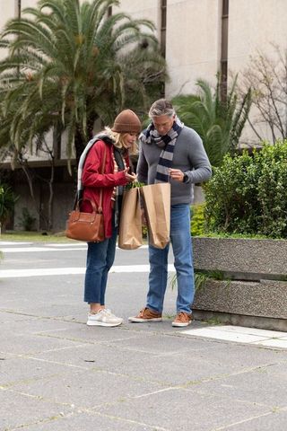 Middle-aged couple checking receipt from brown paper shopping bags on city plaza