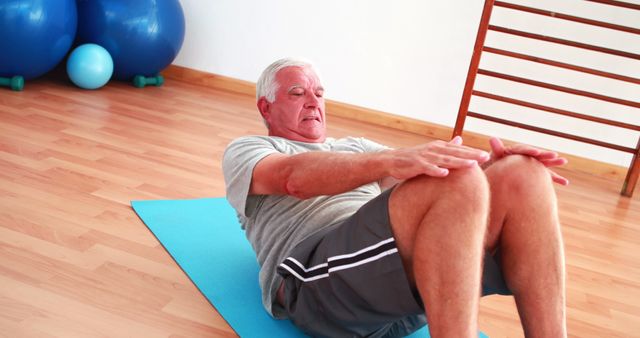 Senior man exercising on yoga mat indoors, performing a sit-up. Useful for promoting senior fitness programs, gym memberships, healthy lifestyle campaigns, and workout routines for elderly individuals.