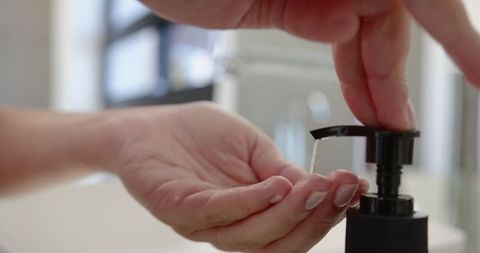 Hands pressing soap dispenser in minimalist bathroom setting