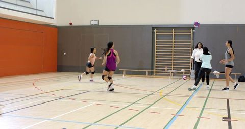 Diverse female teammates practicing volleyball in school gym running spiking during drill