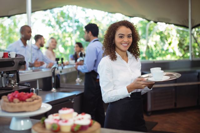 Smiling waitress holding a coffee tray in an outdoor cafe. Ideal for use in hospitality industry promotions, restaurant advertisements, customer service training materials, and cafe marketing campaigns. Highlights professional service and friendly customer interaction.