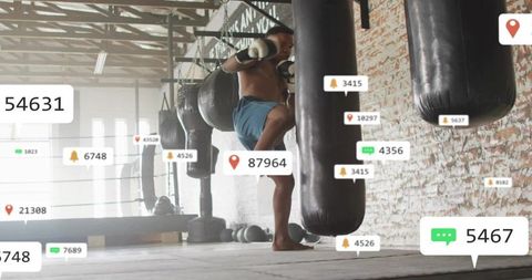 Shirtless boxer kicking heavy bag in industrial gym with social media overlay and daylight