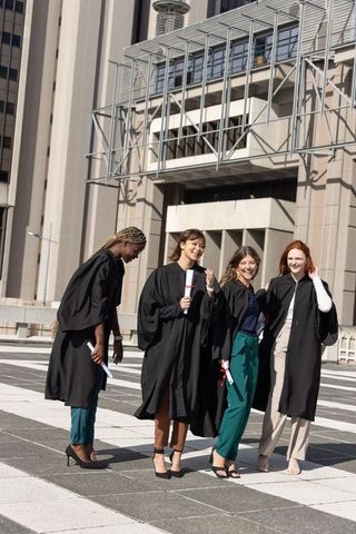 Multicultural female graduates celebrating on urban campus plaza in gowns holding diplomas