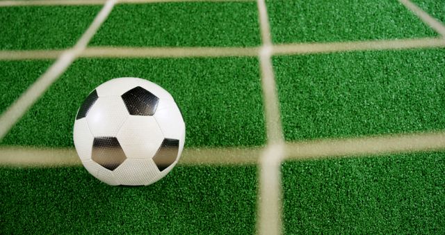 A classic black and white soccer ball rests on a green artificial turf behind a white goal line, with copy space. Capturing the essence of soccer, the image symbolizes the excitement and competitive spirit of the sport.