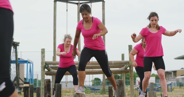 Determined caucasian female friends in pink t shirts crossing logs at bootcamp training. Female fitness, friendship, challenge and healthy lifestyle.