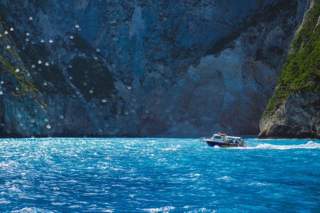 Speed boat cruising through vivid blue coastal water near imposing rocky cliffs. Ideal for use in travel blogs, vacation planning guides, adventure posters, or any media related to ocean activities and coastal landscapes. Perfect for showcasing summer escapes and nautical tourism.