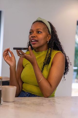 Young african american woman recording voice message on smartphone at kitchen counter