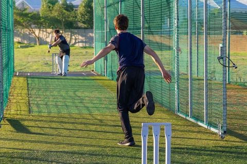 Cricket nets intense training bowler running to bowl while batter defending stumps on turf