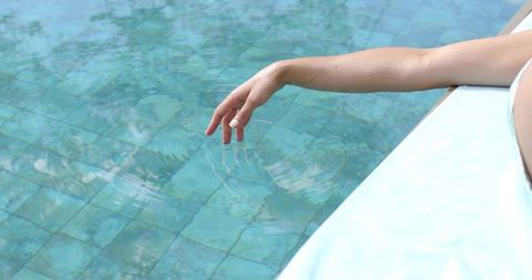 African american woman relaxing poolside touching water creating ripples in mosaic pool