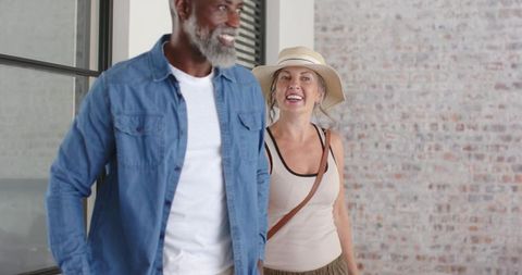Mature couple touring industrial loft, smiling and entering bright brick corridor