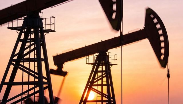 Sunset oil pumpjack silhouette pumping on flat field with walking beam tower