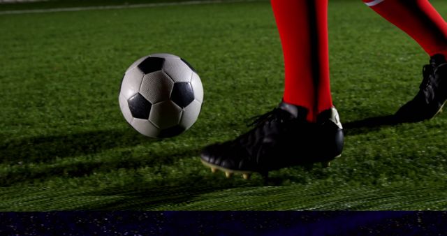 Low section of soccer player and ball on playing field at night 