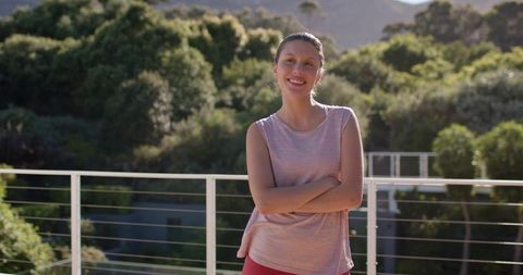 Young african american woman standing on sunlit balcony wearing pink activewear smiling