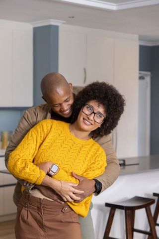 Couple hugging and smiling in modern kitchen showing smartwatches and cozy fashion