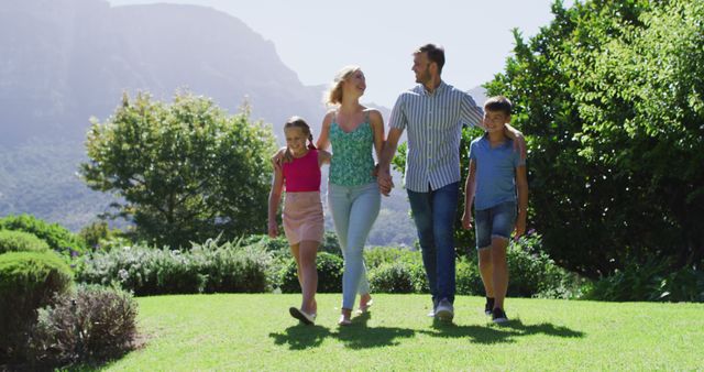 Happy family of four walking together in a beautiful sunlit park. Perfect for depicting family bonding, outdoor activities, healthy lifestyles and nature-loving moments. Ideal for use in advertisements, family lifestyle blogs, and nature-related articles.
