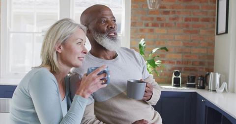 Senior Couple Enjoying Coffee Near Bright Kitchen Window