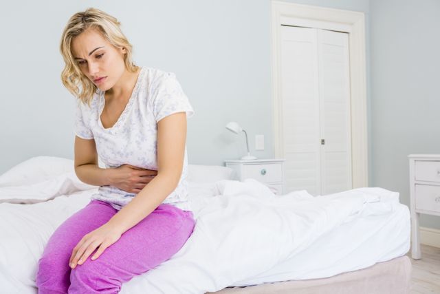 Young woman having stomach pain in bed at bedroom