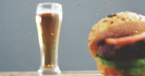 Seeded burger and tall beer glass with golden confetti glittering on wooden table