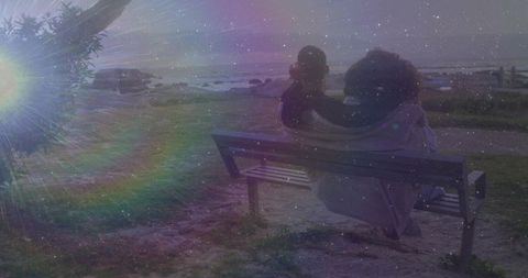 Couple sitting on bench sharing blanket during coastal sunset with lens flare and stars