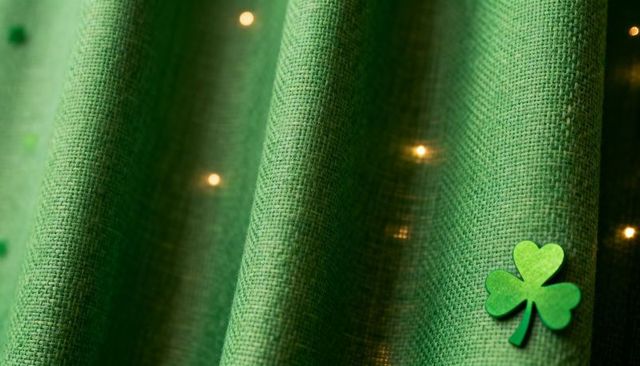 Shamrock resting on textured emerald curtain featuring warm fairy-light bokeh and soft folds