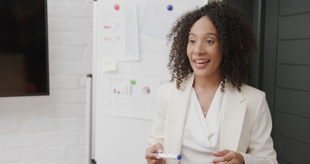 A businesswoman is delivering a presentation in a modern office. She is holding a whiteboard marker and smiling, indicating engagement and confidence. This image can be used for promoting corporate training services, business seminars, leadership courses, and business consulting websites.