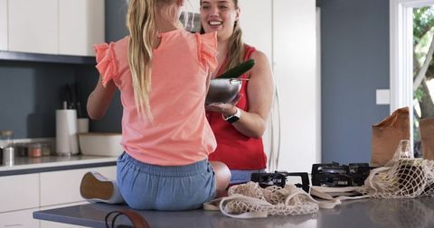 Mother and daughter preparing fresh vegetables on kitchen island, family cooking moment