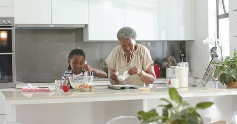 African-american grandmother and granddaughter baking at sunlit modern kitchen island