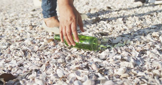 Hand Picking Up Green Bottle from Seashell-Covered Beach Shore - Download Free Stock Images Pikwizard.com