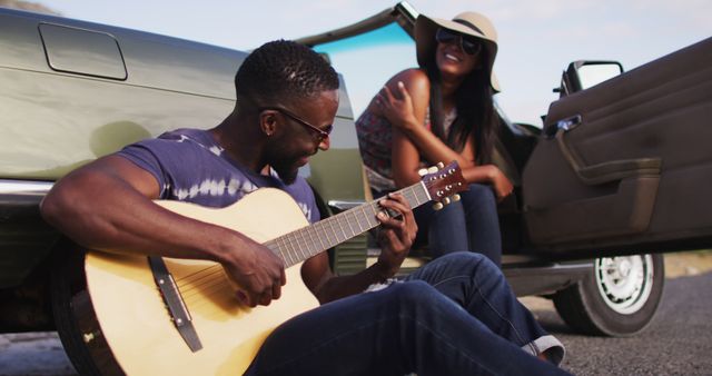 An African American couple enjoying a summer road trip in a convertible car, with a man playing guitar and a woman relaxing while wearing a hat and sunglasses. Perfect for travel advertisements, music and lifestyle blogs, summer campaigns, and inspirational stories emphasizing joy and togetherness.
