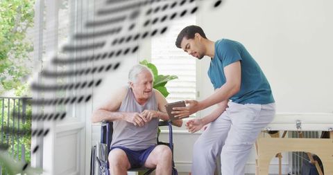 Caregiver guiding senior in wheelchair through tablet-assisted rehab exercises sunlit home