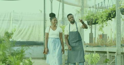 Greenhouse attendant guiding customer through hanging plants and lush potted greenery