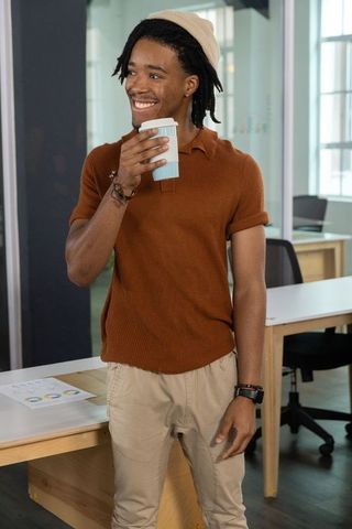 African american man smiling while holding coffee cup in modern coworking office wearing beanie