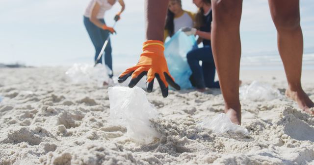 Group of people engaging in beach cleanup activity, removing plastic waste from the sand. They work together wearing gloves and using trash bags. Ideal for promoting environmental initiatives, conservation efforts, community activities or eco-friendly campaigns.
