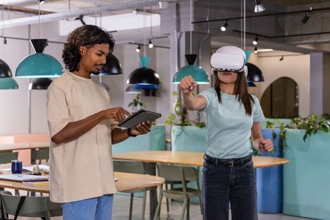 Indian man guiding coworker using vr headset in modern coworking space with teal accents