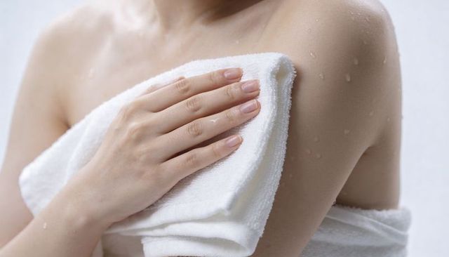 Woman drying wet shoulder with white towel, close-up of moist skin and neat nails