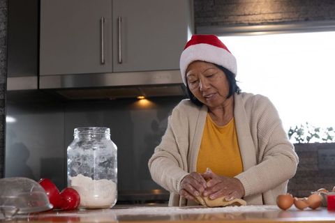 Senior Woman in Santa Hat Kneading Dough in Warm Kitchen